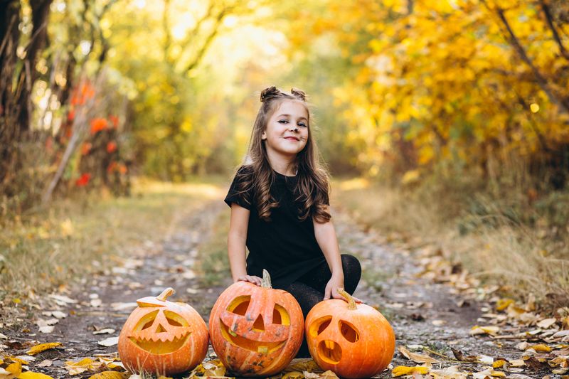 Cute girl dressed in halloween costume outdoors with pumpkins